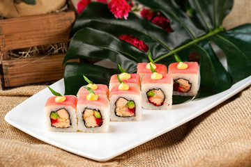 Plate of sushi rolls with tuna, avocado, salmon decorated with flowers at sack cloth background.