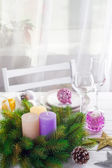 Obraz na płótnie Canvas Christmas wreath with colorful big candles on a table with a Christmas table setting on a white wooden table in front of a light window