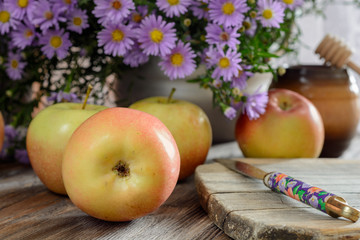 Ripe ruddy apples on a wooden table next to a bouquet of flowers