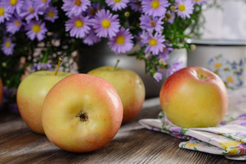 Ripe ruddy apples on a wooden table next to a bouquet of flowers