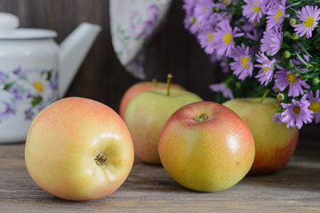 Ripe ruddy apples on a wooden table next to a bouquet of flowers