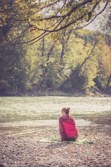 Junge Frau sitzt am Ufer eines Flusses und genießt die Sonne, Hinteransicht