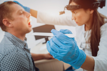 Otolaryngologist examines man's throat with spatula. Medical equipment