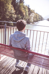 Junger Mann sitzt entspannt auf Spazierbank, Blick auf Fluss und Wälder