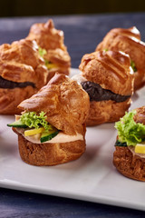 Savory profiteroles with different types of fillings. Salty cakes for snacks. Mini sandwiches, canapes with vegetables, meat, liver, sauce. An exquisite French snack for a buffet at the feast.