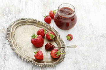 Jar of strawberry jam and ripe fruits.