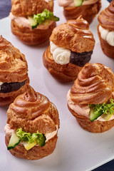 Savory profiteroles with different types of fillings. Salty cakes for snacks. Mini sandwiches, canapes with vegetables, meat, liver, sauce. An exquisite French snack for a buffet at the feast.