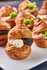 Savory profiteroles with different types of fillings. Salty cakes for snacks. Mini sandwiches, canapes with vegetables, meat, liver, sauce. An exquisite French snack for a buffet at the feast.