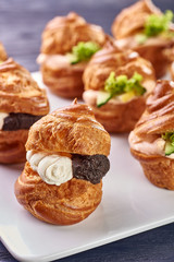 Savory profiteroles with different types of fillings. Salty cakes for snacks. Mini sandwiches, canapes with vegetables, meat, liver, sauce. An exquisite French snack for a buffet at the feast.