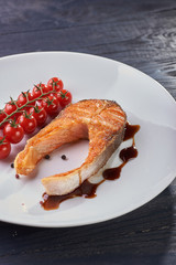 Appetizing expensive salmon steak with a sprig of cherry tomatoes, black fragrant pepper and dark sauce from balsamic vinegar. A simple dish for a festive and casual menu. Source of Omega-3.