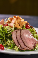 A hearty nice salad for the festive table. Slices of salted meat, bacon, beef, veal, pork from oven, meat sausage, ham. Appetizer from greenery, arugula, mushrooms chanterelles and cherry tomatoes.