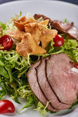 A hearty nice salad for the festive table. Slices of salted meat, bacon, beef, veal, pork from oven, meat sausage, ham. Appetizer from greenery, arugula, mushrooms chanterelles and cherry tomatoes.