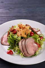 A hearty nice salad for the festive table. Slices of salted meat, bacon, beef, veal, pork from oven, meat sausage, ham. Appetizer from greenery, arugula, mushrooms chanterelles and cherry tomatoes.