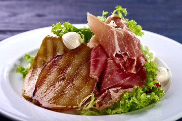Expensive Italian, Spanish, French salad for festive table. Snack from pear, mozzarella, jamon, greens, lettuce, sauce. Cuisine of France, Spain, Italy. Photo of food for menu, cookbook, culinary blog