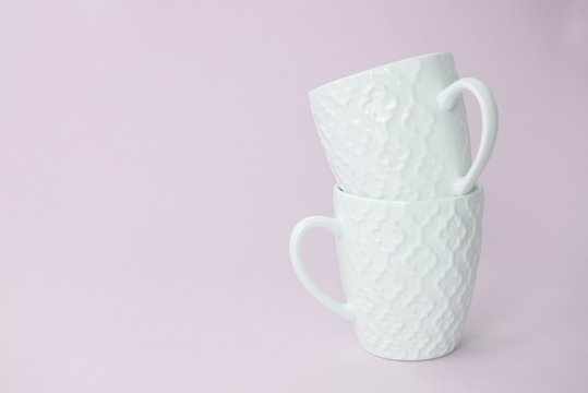 Two white mugs one in the other on pink background