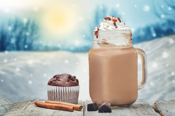 Cup of hot chocolate with whipped cream on a wooden table in a winter forest