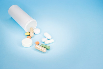 Different pills spilled out of a bottle on a blue background