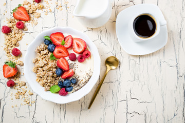 Fototapeta na wymiar Granola with berries, yoghurt and coffee for breakfast. Cereal oats with strawberries, blueberries and raspberries for healthy eating. Top view, copy space