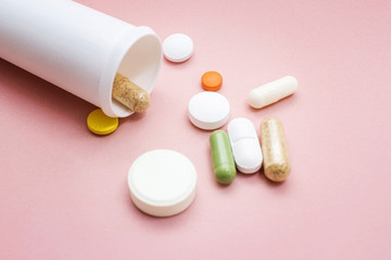 Tablets and pills from a bottle on a pink background