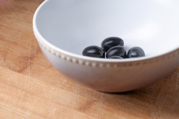 Bowl with some black olives side view. Copyspace on the wooden plate. Diagonal composition, part of the bowl.