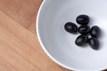 Black olives in bowl from above view, copyspace on wooden plate
