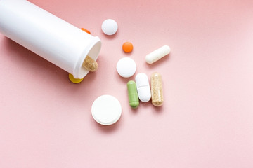Tablets and pills from a bottle on a pink background