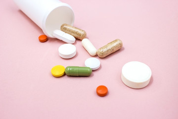 Tablets and pills from a bottle on a pink background