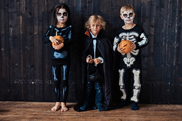 Three cute kids in scary costumes during Halloween party in an old house.