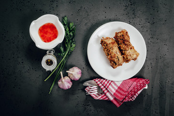 Top view of spring rolls on a white plate. Spring rolls, springroll dressing and food ingredients on a dark, stone counter top. The concept of serving dishes, eating spring rolls.