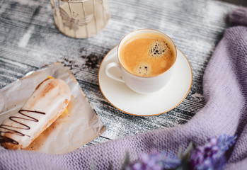Cup of hot coffee, eclair and flowers on rustic wooden table, closeup photo warm sweater, winter...