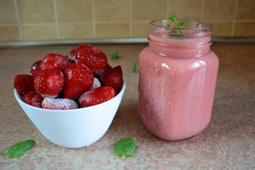 Smoothie with frozen strawberries and natural yoghurt decorated with a sprig of mint, frozen strawberries in a bowl