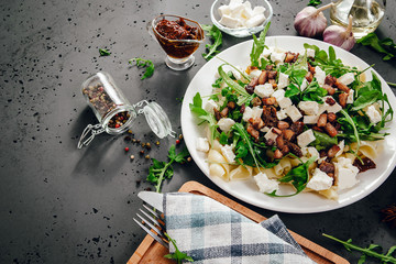 Side view of a plate with food. A dish of pasta, rucola and spices, next to the ingredients of food, garlic, tomatoes on a stone, dark countertop. The concept of preparing food.
