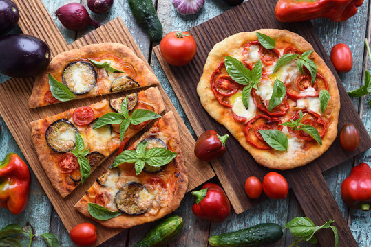 Healthy vegetarian food. Rustic pizzas with eggplants, tomatoes and bell peppers on oak cutting boards served with raw ingredients