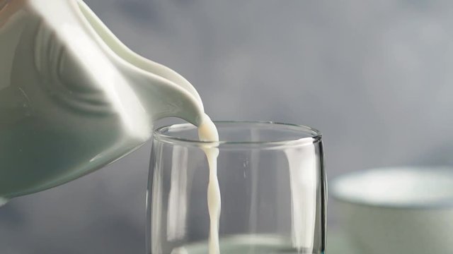 Pouring milk from a pitcher in a glass on gray background. Closeup