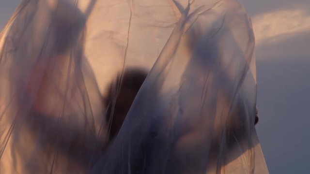 Slow Motion Portrait Shot Of A Woman Trying To Fly Wrapped In Plastic Foil And Failing At Sunset
