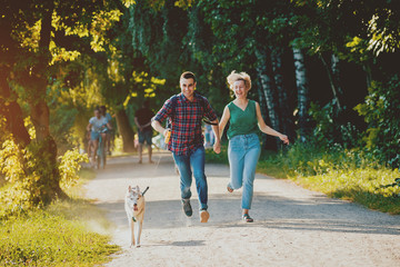 Dog with owners spend a day at the park. Young couple and husky running, playing and having fun.