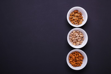 Three bowls with different nuts on a black table