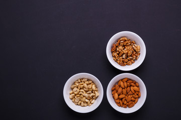 Three bowls with different nuts on a black table