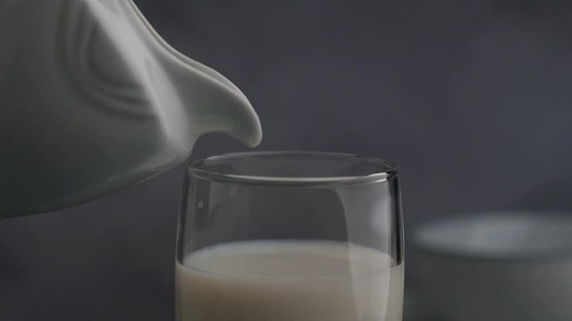 Pouring milk from a pitcher in a glass on gray background. Closeup