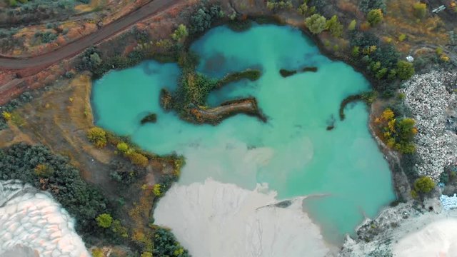 Turquoise water in lake near chalk quarry and industrial digging machinery, top view