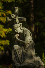 Fototapeta na wymiar Sculpture of a Woman kneeling on a Cross - Tombstone on a Cemetery in Berlin, Germany