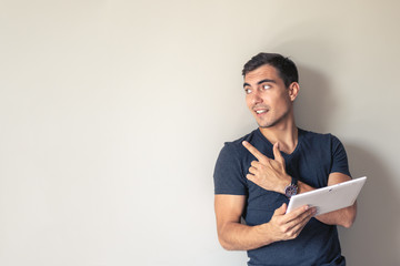 Man for conceptual design. A handsome young man uses a tablet standing at a gray wall, copy space