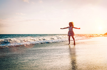 Happy little girl running inside water spreading her hands up on the beach - Baby having fun making splashing in the sea - Child, youth, happiness concept
