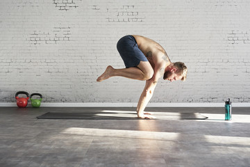 Fototapeta premium Muscular tattooed athlete exercising yoga asana push up inside in sunny sport club. Fit shirtless male fitness model..
