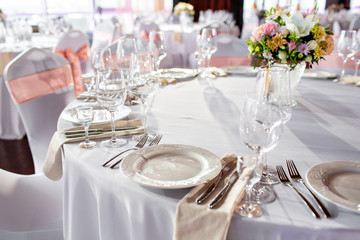 Round table at a luxury wedding reception. Beautiful flowers on the table. Serving dishes, glass glasses, waiters work,