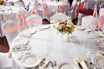 Round table at a luxury wedding reception. Beautiful flowers on the table. Serving dishes, glass glasses, waiters work,