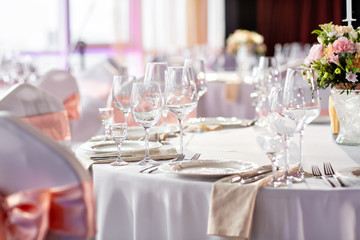 Round table at a luxury wedding reception. Beautiful flowers on the table. Serving dishes, glass glasses, waiters work,