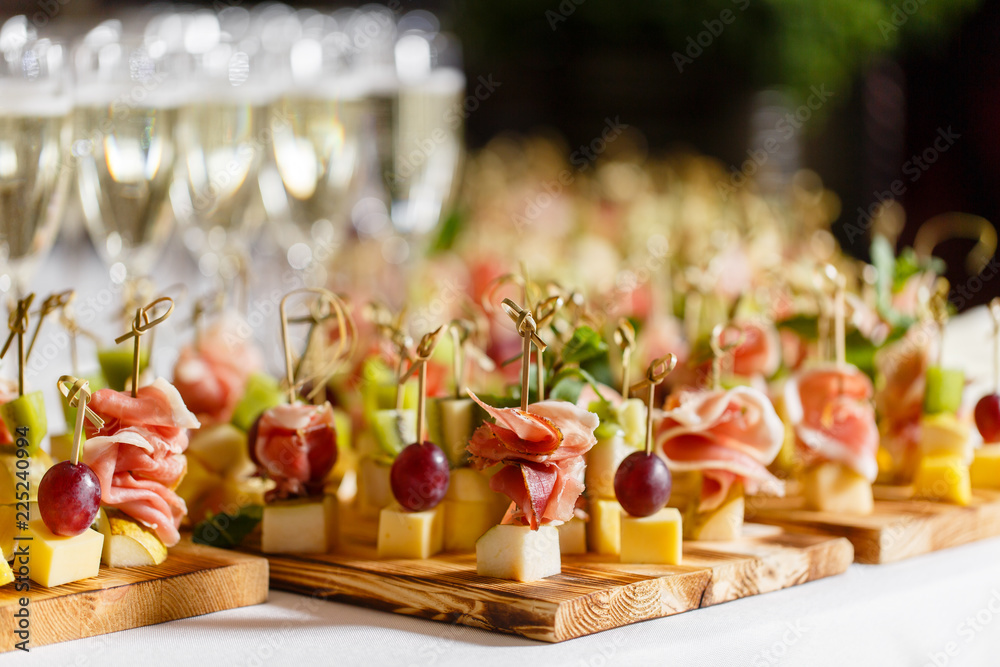 Wall mural the buffet at the reception. Glasses of wine and champagne. Assortment of canapes on wooden board. Banquet service. catering food, snacks with cheese, jamon, prosciutto and fruit