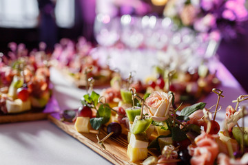 the buffet at the reception. Assortment of canapes on wooden board. Banquet service. catering food, snacks with cheese, jamon, prosciutto and fruit