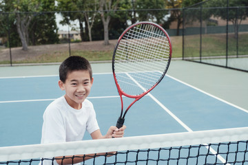 Young tween Asian boy tennis player on outdoor blue court